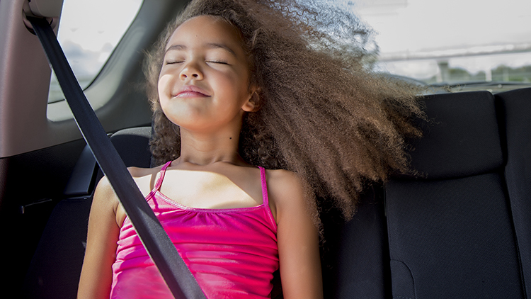 Waist-up view of a 6-7 year old mixed race girl sitting in the back seat of a car and enjoying the wind blowing in her hair