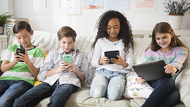 Children using cell phones and digital tablets on sofa